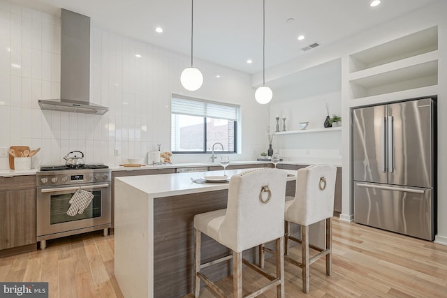 kitchen with a center island, a kitchen breakfast bar, pendant lighting, stainless steel appliances, and wall chimney range hood