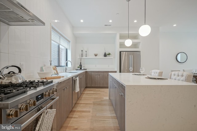 kitchen with decorative light fixtures, ventilation hood, sink, a large island with sink, and high end appliances