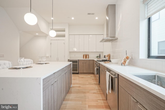 kitchen featuring a center island, white cabinets, pendant lighting, stainless steel appliances, and wall chimney range hood