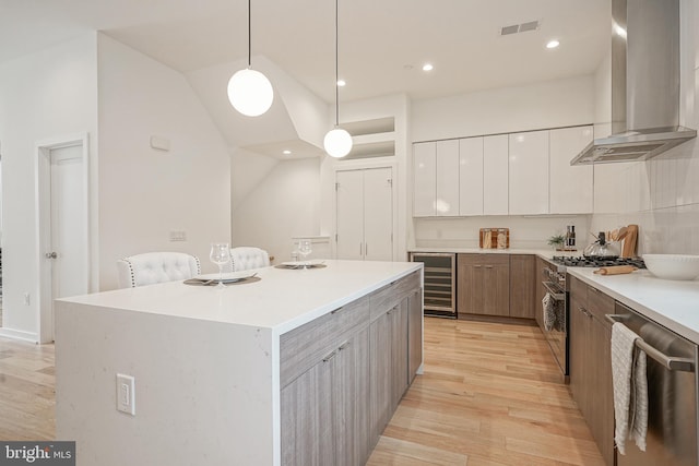 kitchen with appliances with stainless steel finishes, decorative light fixtures, white cabinetry, beverage cooler, and wall chimney range hood