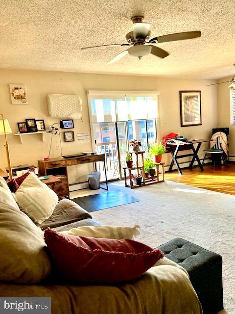 living room featuring a textured ceiling, ceiling fan, and a baseboard heating unit