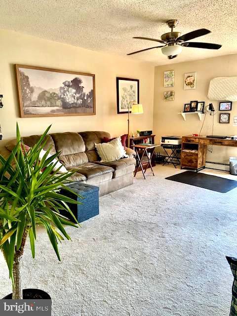 living room with ceiling fan, carpet flooring, and a textured ceiling