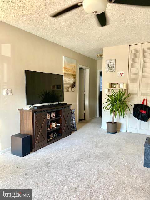 carpeted living room featuring ceiling fan and a textured ceiling