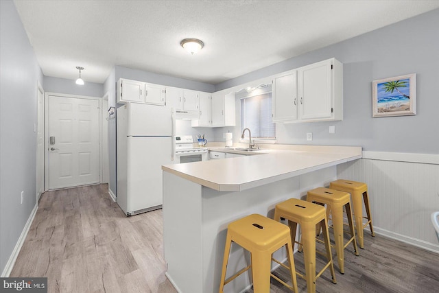 kitchen with a breakfast bar area, white cabinets, light hardwood / wood-style floors, kitchen peninsula, and white appliances