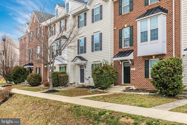 townhome / multi-family property with a standing seam roof, brick siding, metal roof, and a front lawn