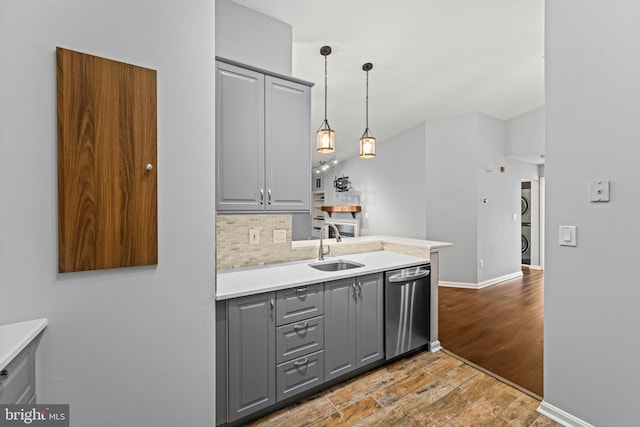 kitchen featuring stacked washer / drying machine, sink, gray cabinets, dishwasher, and pendant lighting