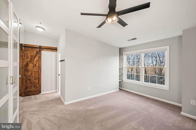 carpeted empty room with ceiling fan and a barn door