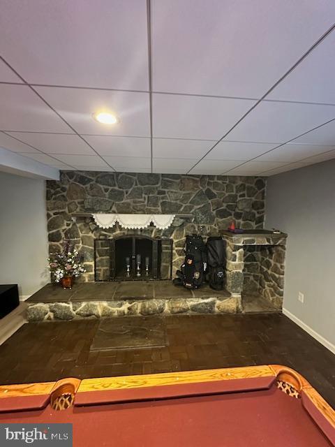 interior space featuring wood-type flooring, a stone fireplace, and a drop ceiling