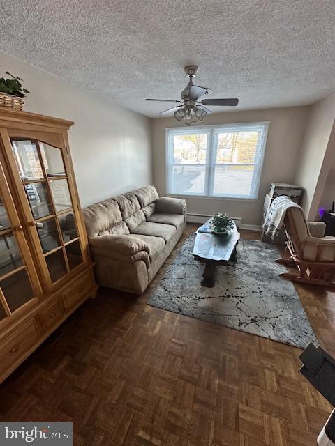 living room with dark parquet flooring, ceiling fan, a textured ceiling, and baseboard heating