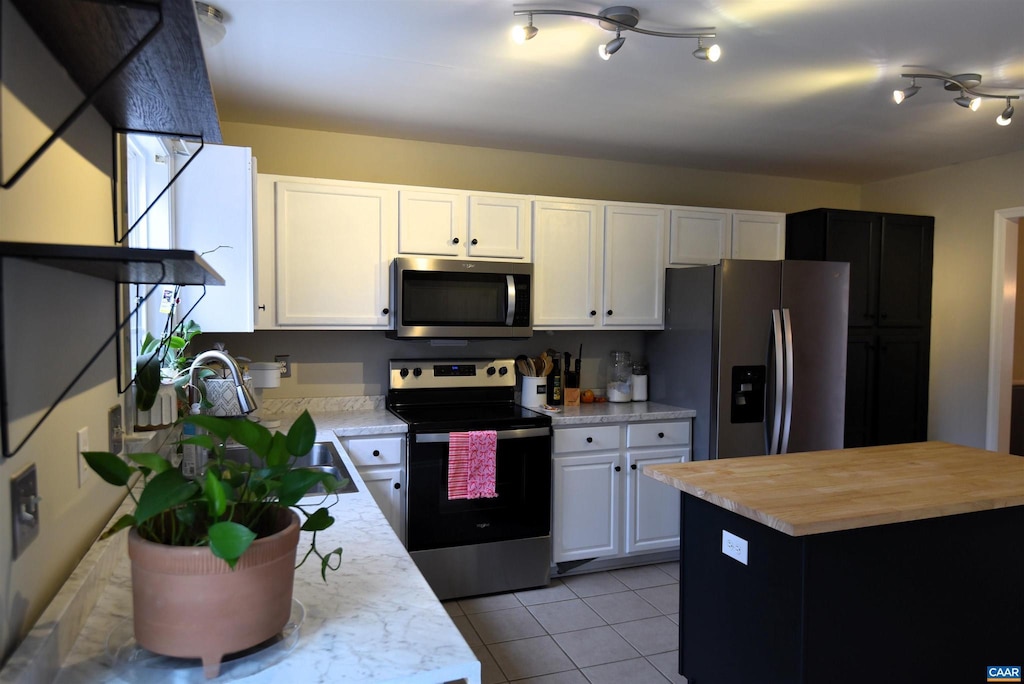 kitchen featuring light tile patterned floors, a center island, white cabinets, and appliances with stainless steel finishes