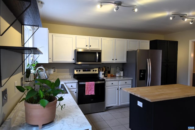 kitchen featuring light tile patterned floors, a center island, white cabinets, and appliances with stainless steel finishes