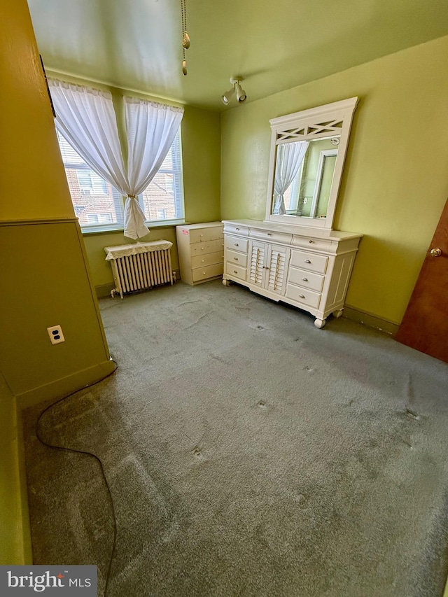 unfurnished bedroom with track lighting, radiator heating unit, and light colored carpet