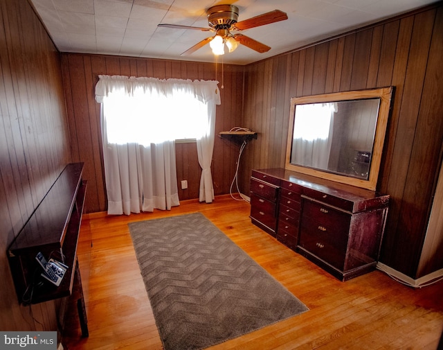 interior space featuring a ceiling fan, wooden walls, and light wood finished floors