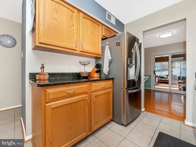 kitchen with stainless steel refrigerator with ice dispenser, light tile patterned flooring, and dark stone countertops