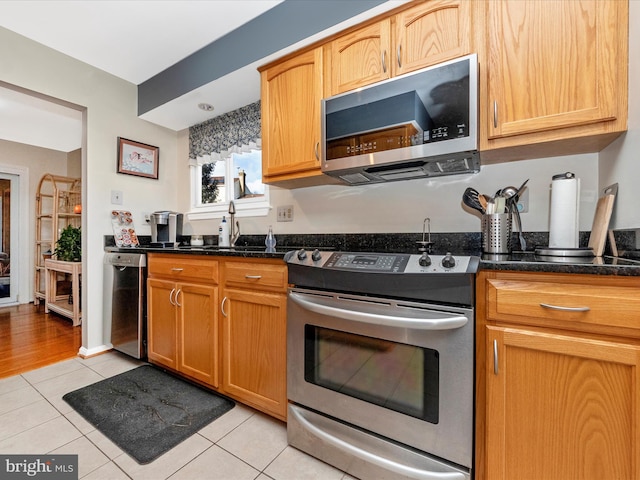 kitchen featuring light tile patterned flooring, stainless steel appliances, and dark stone countertops