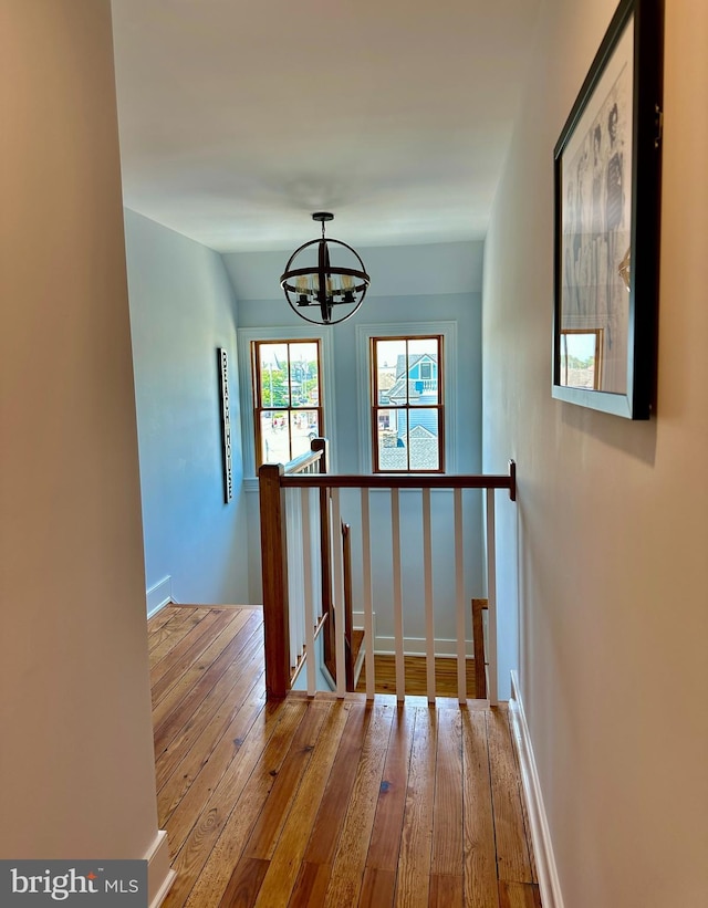 corridor with wood-type flooring and an inviting chandelier