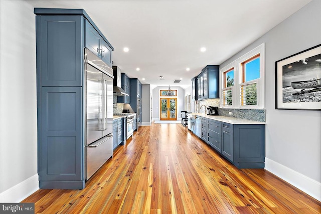 kitchen featuring blue cabinetry, high quality appliances, decorative backsplash, and wall chimney range hood