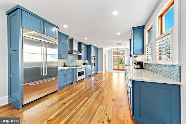 kitchen featuring wall chimney exhaust hood, blue cabinets, light hardwood / wood-style flooring, and premium appliances