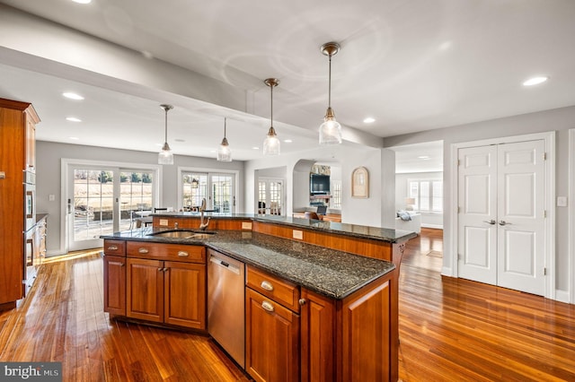 kitchen with dark stone counters, open floor plan, hanging light fixtures, dishwasher, and a center island with sink