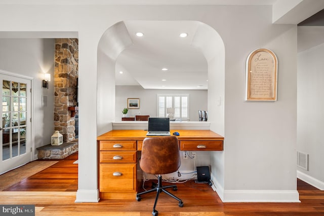 office with baseboards, visible vents, arched walkways, and wood finished floors