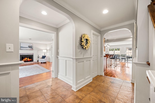 hall with arched walkways, recessed lighting, a decorative wall, ornamental molding, and wainscoting