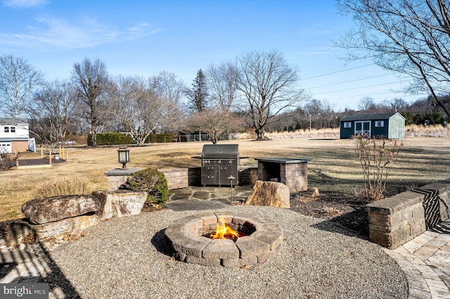 view of patio / terrace featuring an outdoor fire pit, a grill, an outdoor structure, and a storage shed