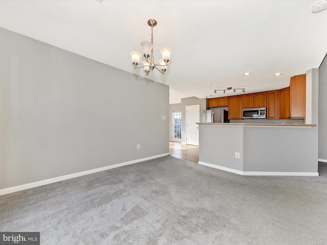 unfurnished living room with light colored carpet, rail lighting, and a chandelier