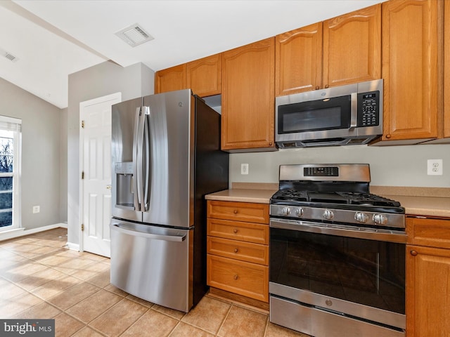 kitchen featuring appliances with stainless steel finishes, vaulted ceiling, and light tile patterned floors