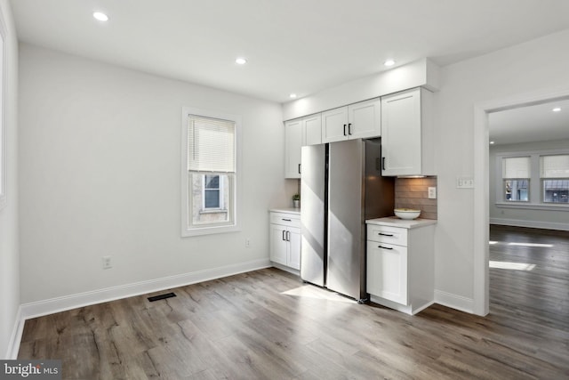 kitchen featuring stainless steel fridge, a wealth of natural light, white cabinets, and decorative backsplash