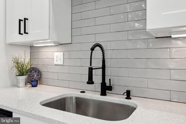 interior details featuring light stone counters, sink, tasteful backsplash, and white cabinets