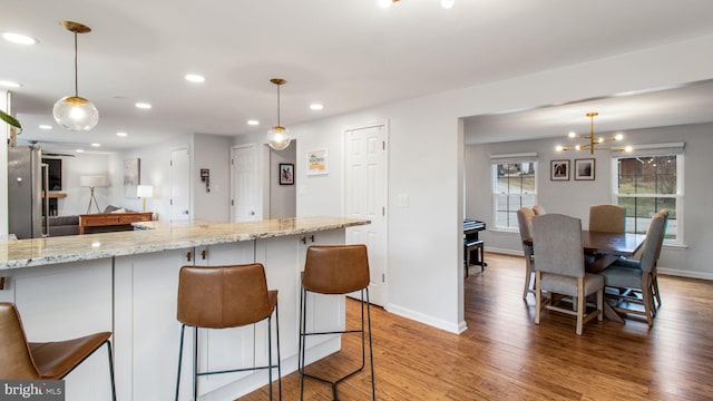 kitchen with pendant lighting, a kitchen breakfast bar, light stone countertops, and hardwood / wood-style floors