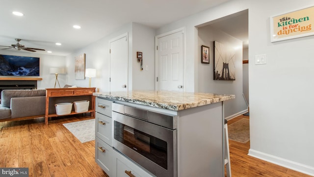 kitchen featuring gray cabinets, a kitchen island, stainless steel microwave, light hardwood / wood-style floors, and light stone countertops