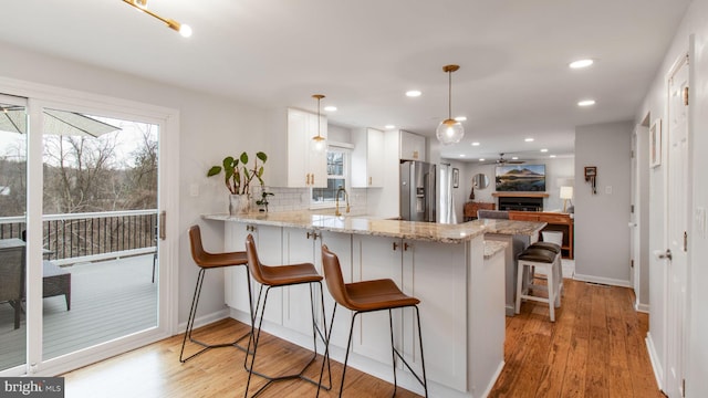 kitchen with a breakfast bar area, white cabinetry, stainless steel fridge with ice dispenser, decorative light fixtures, and kitchen peninsula