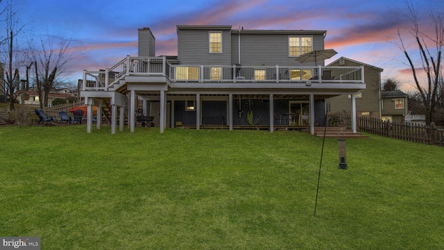 back house at dusk featuring a wooden deck and a lawn