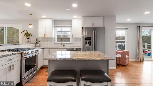 kitchen featuring sink, white cabinetry, light stone counters, hanging light fixtures, and appliances with stainless steel finishes