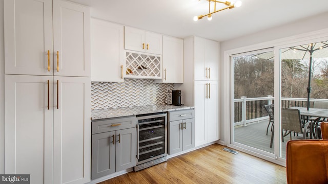 bar with gray cabinetry, white cabinetry, tasteful backsplash, light hardwood / wood-style flooring, and beverage cooler