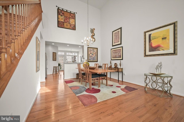 dining room with hardwood / wood-style flooring, a towering ceiling, and an inviting chandelier