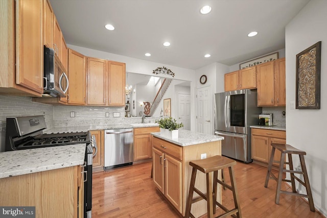 kitchen featuring sink, appliances with stainless steel finishes, a kitchen island, a kitchen bar, and light wood-type flooring