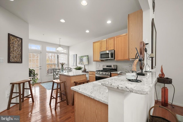 kitchen with a kitchen breakfast bar, kitchen peninsula, a kitchen island, stainless steel appliances, and light stone countertops