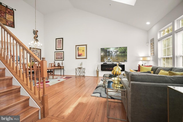 living room featuring a notable chandelier, wood-type flooring, high vaulted ceiling, and a skylight