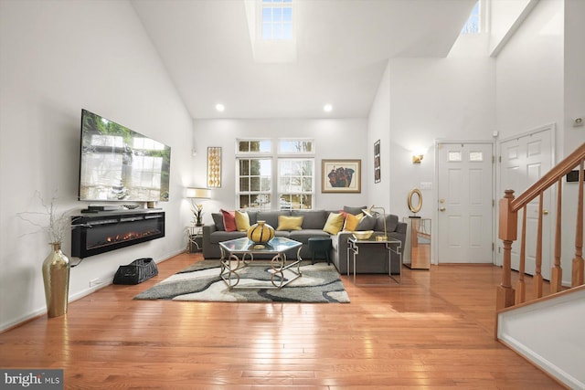 living room featuring high vaulted ceiling, light wood-type flooring, and a skylight