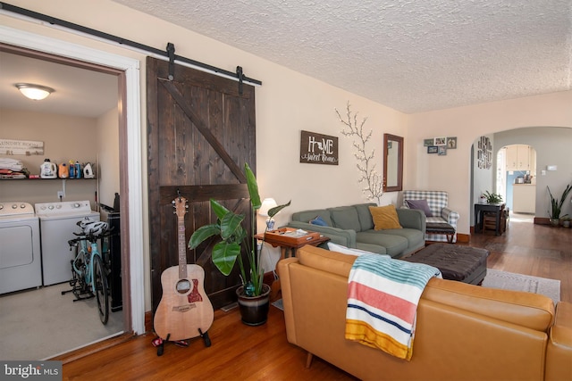 living room featuring arched walkways, a textured ceiling, independent washer and dryer, and wood finished floors