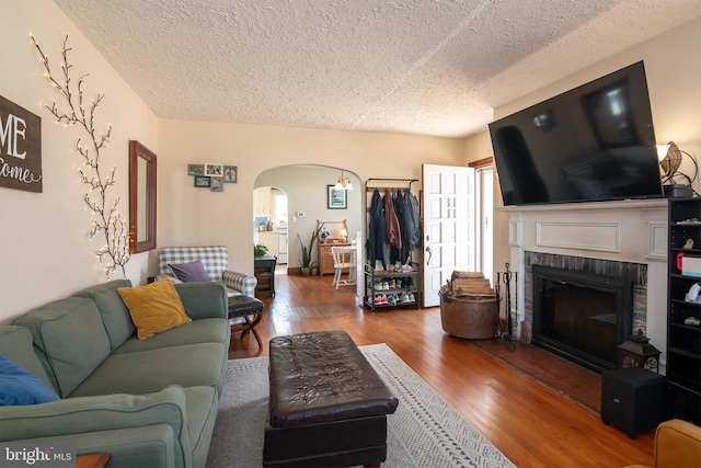 living room with arched walkways, a fireplace, a textured ceiling, and wood finished floors