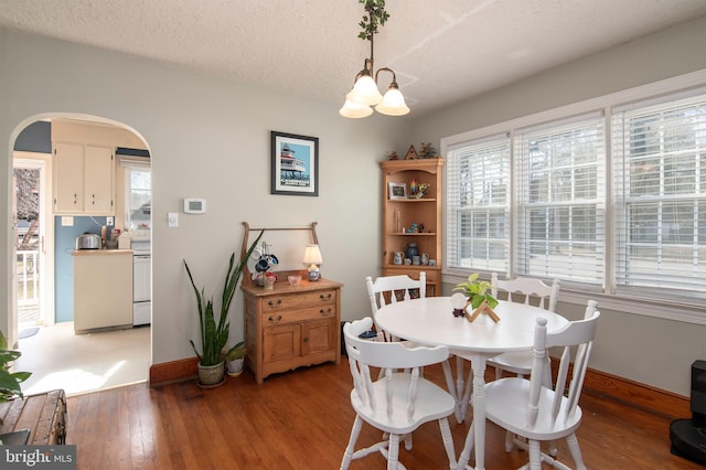 dining space featuring light wood-type flooring, baseboards, arched walkways, and a textured ceiling