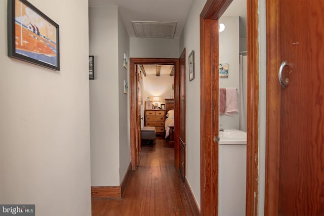 hall featuring visible vents, baseboards, and wood finished floors