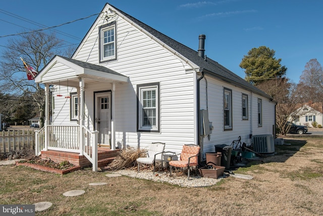 exterior space with central AC unit, roof with shingles, a front yard, and fence