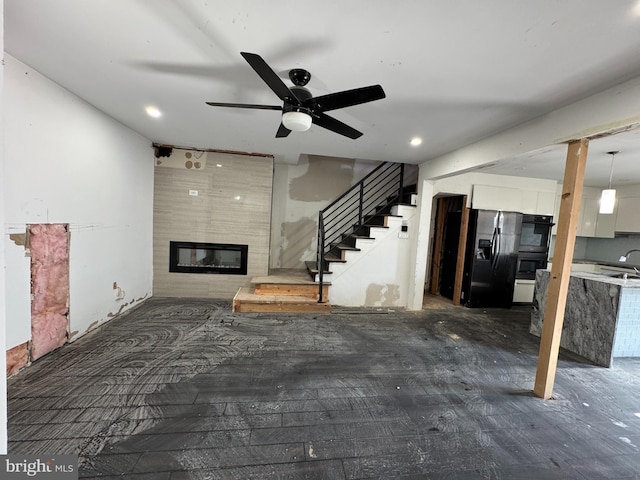 unfurnished living room featuring a large fireplace, sink, and ceiling fan