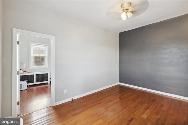 empty room featuring ceiling fan, radiator heating unit, and wood-type flooring