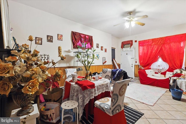 dining area with light tile patterned floors, ceiling fan, and wood walls