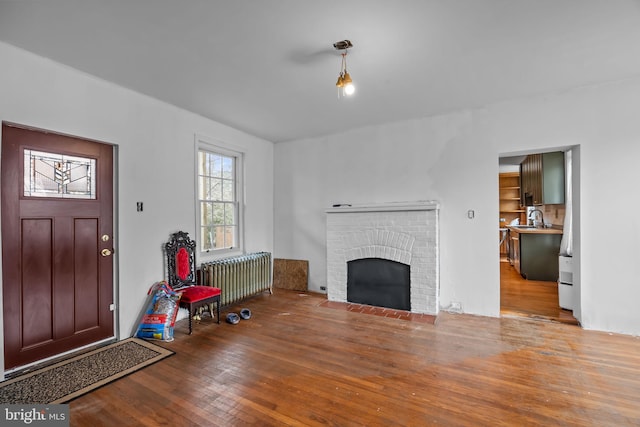 living room with radiator heating unit, a fireplace, sink, and light wood-type flooring